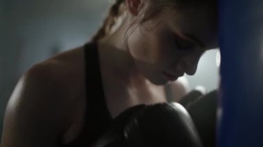 Kadın gücü, yorgun kadın dövüşçü boks salonunda ağır antrenman yapan, kum torbasına baskı yapıyor..