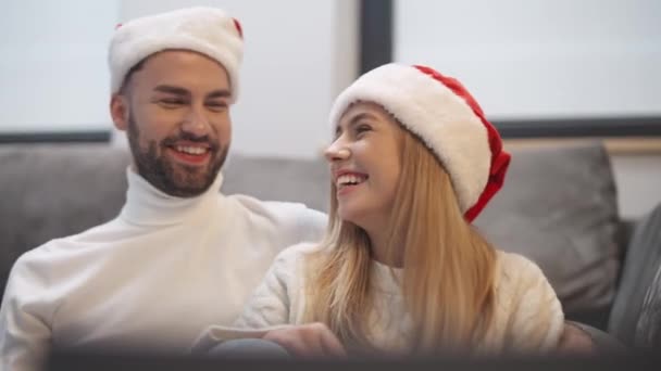クリスマス サンタクロースの帽子の若いカップルはリビングルームの床に座って ラップトップを使用してビデオ通話で親戚と通信します 冬の休日 — ストック動画