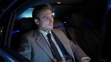 Hareket halindeki bir arabada oturan ve viski içen genç bir işadamının portresi takım elbiseli bir adam bir iş arabasının arkasında oturuyor, gece gezintisi..