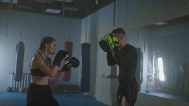 Kadın boksör yumrukları ve savunmayı eğitiyor, odaklanma eldiveni yumrukluyor, antrenman günü boks salonunda koçla antrenman yapıyor, 4K Slow Motion.