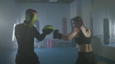 Kadın boksör hızlı yumruklarını, odaklanma eldivenlerini, antrenman günlerini boks salonunda antrenman günlerini, genç kadın hızlı saldırıyor..