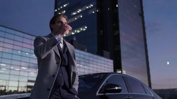 一个快乐的商人站在一辆商用车旁喝咖啡 身穿西服的高级经理 晚上时分 背景中的写字楼 手持的画像 — 图库视频影像