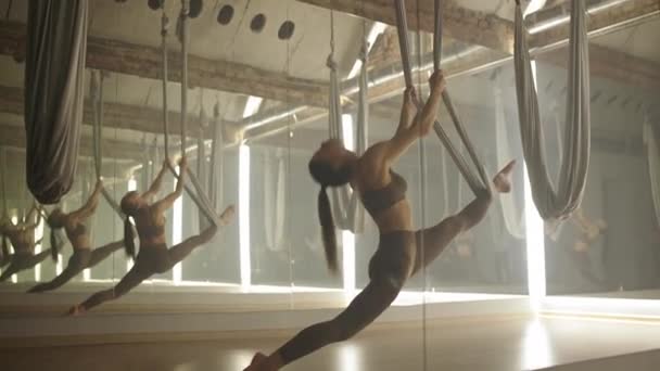 年轻女人在一个有镜子的房间里做伸展运动 女人在一个有瑜伽元素的房间里做伸展运动 漂亮的舞蹈是用织物环跳的 — 图库视频影像
