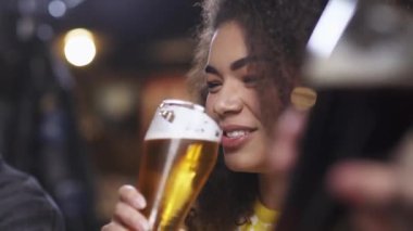 Futbol şampiyonası sırasında barda arkadaşlarıyla buluşan koyu tenli bir kadın bira içer ve arkadaşlarıyla iletişim kurar..