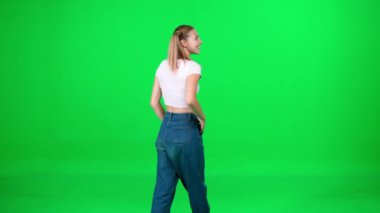 Yeşil arka planda yürüyen genç bir kadın, yoldan geçen bir yürüyüşçü, krom anahtar şablonu, beyaz tişörtlü ve mavi kotlu bir kadın..