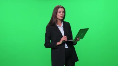 Takım elbiseli kadın öğretim görevlisi seyircilere sesleniyor ve yeşil arka planda dizüstü bilgisayar kullanarak konferans veriyor..