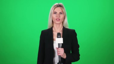 Takım elbiseli kadın muhabir kameraya bakar ve yeşil arka plandaki bir mikrofona konuşur, TV haber ajansları için şablon, iş yerindeki gazeteci, kromakey.