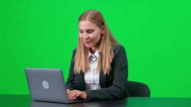 Takım elbiseli neşeli bir iş kadını masasında oturuyor ve bir dizüstü bilgisayar üzerinde çalışıyor, müdür iyi bir anlaşma yapıyor, yeşil arka plan, kromakey şablonu..