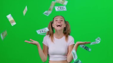 Beyaz kadın yeşil odada duruyor ve kameraya bakıyor, genç kadın büyük bir zaferle mutlu, dolar ve avro banknotları havada uçuşuyor, kroma anahtar arka plan, pozitif duygular, 4k yavaş