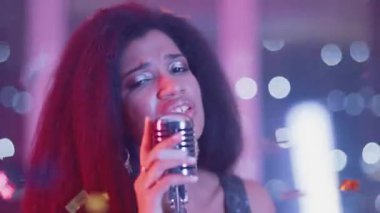 Lüks Parti, gece kulübünde şarkı söyleyen Afrikalı genç bir kadının portresi, neon ışıkta yüzlü bir kadının yakın çekimi, sahnede şarkıcı..