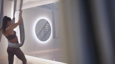 Yavaş çekim, kadın ayna odasında yoga yapıyor, esnek kadın yoga elementleriyle güzel bir dans ediyor, kumaş iplerle odada dans ediyor..