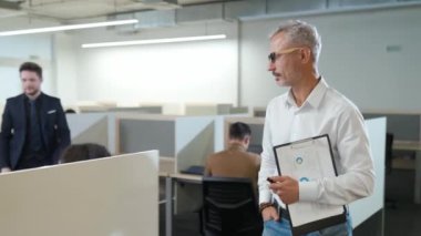 Uluslararası yönetim ekibi açık alanda çalışıyor, genel müdür ofiste dolaşıyor ve iş arkadaşlarıyla iletişim kuruyor..