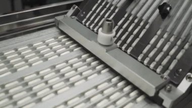 İlaç ve uyuşturucu üretimi, çok sayıda hareket halindeki kapsül, taşıyıcıdaki beyaz tabletler, otomatikleştirilmiş üretim hattı.