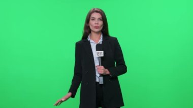 Takım elbiseli kadın muhabir kameraya bakar ve yeşil arka plandaki bir mikrofona konuşur, TV haber ajansları için şablon, iş yerindeki gazeteci, flaş haber.
