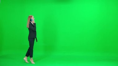 Takım elbiseli bir iş kadını, krom anahtar arka planda yürüyor, akıllı telefon kullanan ve cep telefonuyla konuşan bir kadın, yeşil arka plan, kromakey şablonu.