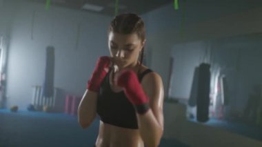 Kadın gücü, genç kadın boksör savaş duruşu yapıyor ve kameraya bakıyor, ciddi bir bakış..