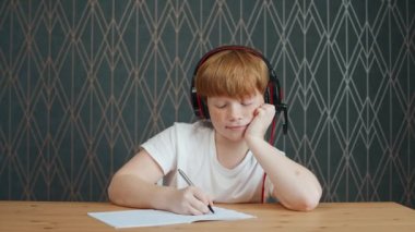 Evde eğitim videosu, oturma odasında işyerinde oturan kızıl saçlı çocuk ve evde kendini izole bir şekilde çalışmak için webcam kullanıyor, sıkılmış tembel çocuk derslerine odaklanamıyor..