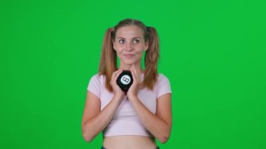 Beyaz kadın yeşil odada duruyor ve kameraya bakıyor, genç kadın tahmin topu kullanarak dilek diliyor, bir oyun oynuyor, krom anahtar arka plan, başarısızlık duyguları..