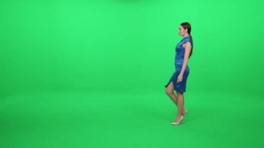 Mavi elbiseli, yeşil arka planda yürüyen zarif genç bir kadın, bir krom şablon, poz veren kadın oyuncu..