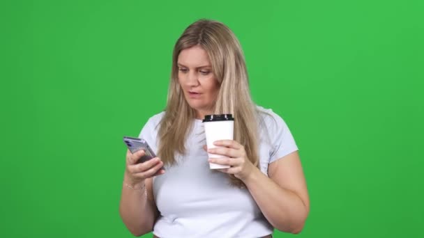 クロメイクの背景に立っている白いTシャツの女性 スマートフォンと飲み物コーヒーを使用して テキストとインターネットをサーフィン 緑の背景 染色体テンプレート — ストック動画