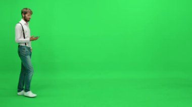 Yoldan geçen takım elbiseli bir işadamı yeşil arka planda yürüyor ve akıllı bir telefonla konuşuyor, kromatonda şablon çiziyor..