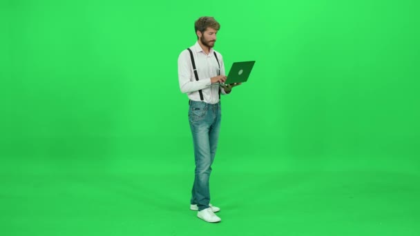 若いアートディレクターは ノートパソコンで動作し タイピングし 外出先でラップトップを使用しています 緑の背景 クロマキーテンプレート — ストック動画