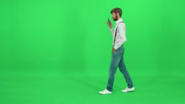 Yoldan geçen takım elbiseli bir işadamı yeşil arka planda yürüyor ve akıllı bir telefonla konuşuyor, kromatonda şablon çiziyor..