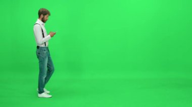 Yoldan geçen beyaz gömlekli adam yeşil arka planda yürüyor ve bir cep telefonuyla konuşuyor, bir kromatonda şablon çiziyor..
