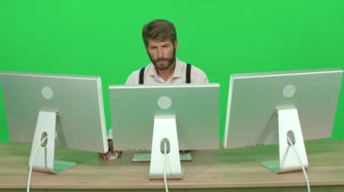 Masada otururken bilgisayar üzerinde çalışan odaklanmış geliştirici, yeşil arkaplan, monitörlerin arkasında çalışan bir adam, kroma anahtar şablonu, arka görünüm.