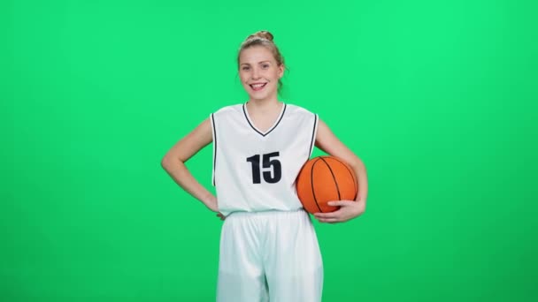 快乐的女运动员 骑着铬钥匙 篮球运动员把球扔在自己的手里 职业篮球运动员在室内操场上 绿色背景 — 图库视频影像
