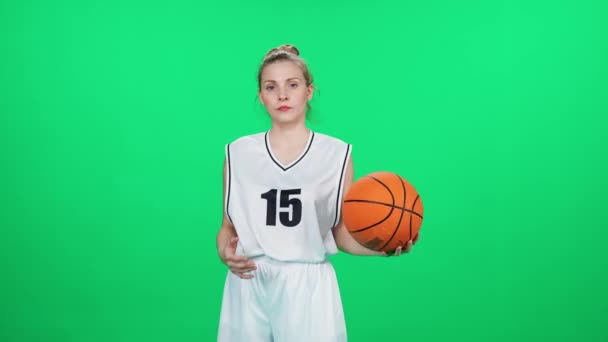 漂亮的女足骑着铬钥匙 篮球运动员把球扔在手中 职业篮球运动员在室内操场上 背景是绿色的 — 图库视频影像