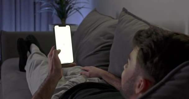 Homem Deitado Sofá Sala Estar Descansa Sofá Usa Smartphone Percorra — Vídeo de Stock