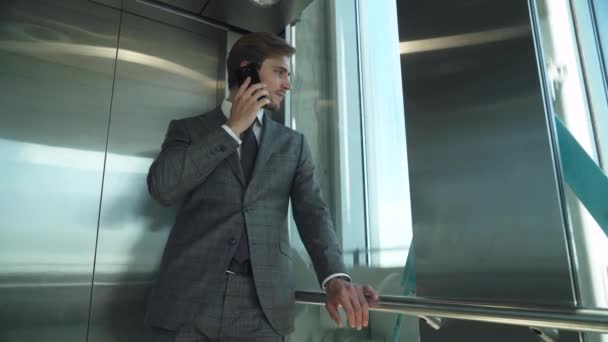 ビジネスマン 若いトップマネージャーはエレベーターのトップに行き 携帯電話で話し 高層ビルのパノラマエレベーターに乗ります — ストック動画