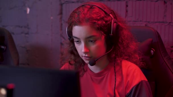 年轻的女玩家头戴耳机 玩电子游戏 与队员 网络游戏运动员 电脑俱乐部的珊瑚霓虹灯进行交流 — 图库视频影像