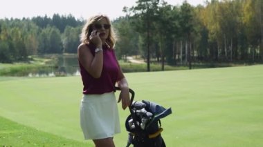 Yaz günü, bir kadın orman bölgesinde golf sahasının yakınında cep telefonuyla konuşuyor..