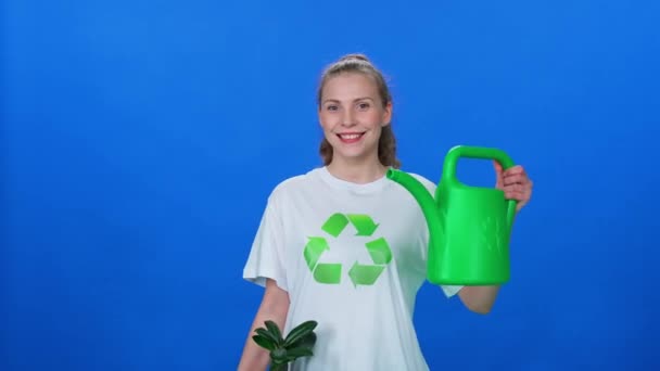 生态学 漂亮的女性生态活动家看着摄像机 手里拿着一个浇灌罐 在蓝色的背景 模板上播种 绿化了整个地球 — 图库视频影像