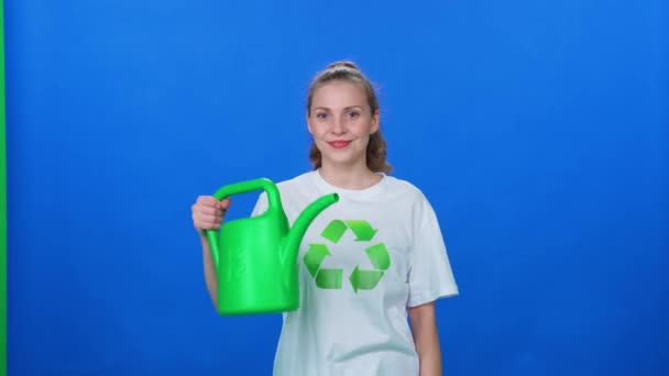 女性生态活动家看着摄像机 手里拿着一个水壶 放在蓝色的背景 模板上 绿化着整个地球 — 图库视频影像