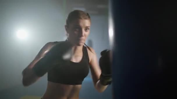 女性のパワー 女性の戦闘機はパンチバッグを打ち 彼のパンチを訓練し ボクシングジムでトレーニング日 女性は速く 映画の照明を打つ — ストック動画