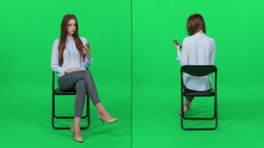 Ofis koltuğunda oturan açık mavi gömlekli zarif bir kadın sosyal ağları, yeşil geçmişi, bekleme sürecini video kolajını kontrol etmek için akıllı telefon kullanıyor..