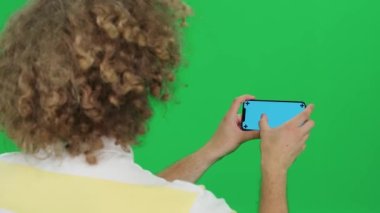 Genç adam akıllı telefon kullanır, görüntüler arasında kayar ve mavi ekran boyunca kayar, yeşil arka plan, yatay görüş, kromakey şablonu.