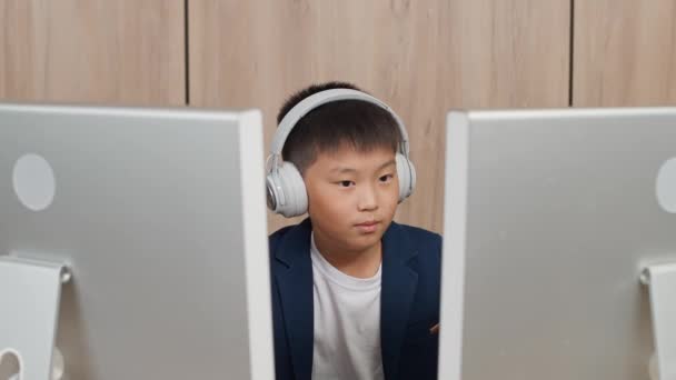 在个人电脑上工作的亚洲男孩坐在家里的书桌前 而在网上工作和学习的男孩则坐在显示器后面 形同虚设 — 图库视频影像
