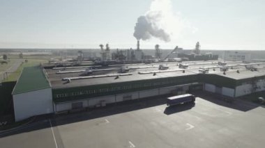 Endüstriyel arazi, büyük ahşap işleme fabrikası, yükseklikten gelen boru ve tankların manzarası, endüstriyel binalar, borulardan gelen duman, lojistik deposu..