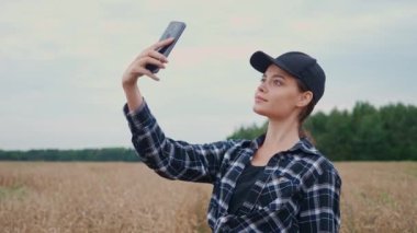 Kırsal kesimde, güzel bir kadın çiftçi çavdar tarlasında dikiliyor ve akıllı bir telefonla fotoğraf çekiyor, bitkileri araştırıyor..