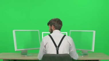 Bir masada otururken bilgisayar üzerinde çalışan yazılım geliştiricisi, yeşil arkaplan, monitörlerin arkasında çalışan bir adam, kroma anahtar şablonu, arka görünüm.