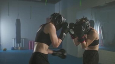 Ağır çekimde, koruyucu kask takan iki kadın dövüşçünün dövüşü, boks salonunda antrenman, kadın antrenman defansı ve savaş alanında bir dizi yumruk..