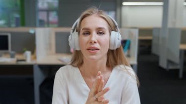 Uluslararası ofis alanının arka planında neşeli bir kadın tasarımcının portresi, kulaklıklı genç bir kadın video ile iletişim kuruyor, kameraya bakıyor, şablon çiziyor..