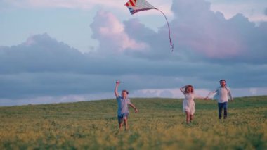 Yaz zamanı. Açık hava eğlencesi, ailesiyle birlikte sahada koşan bir çocuk bir uçurtma fırlatıyor, doğada genç bir aile, gün batımı saati, 4k ağır çekim.
