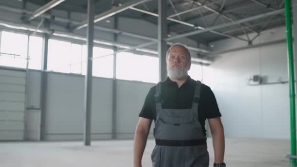 一个头发灰白的成年工人穿过仓库 一个工作的工程师穿过一个空旷的物流仓库 电影般的照明 — 图库视频影像