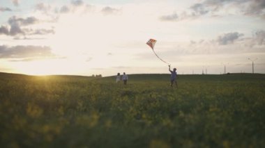 Açık hava eğlencesi yapan genç bir aile, anne babasıyla birlikte sahada koşan bir çocuk bir uçurtma fırlatıyor, doğada genç bir aile, gün batımında..