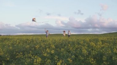 Açık hava eğlencesi yapan genç bir aile, anne babasıyla birlikte sahada koşan bir çocuk bir uçurtma fırlatıyor, doğada genç bir aile, gün batımında..